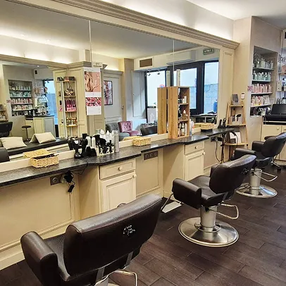 Salon de coiffure moderne avec trois sièges, grands miroirs et produits.