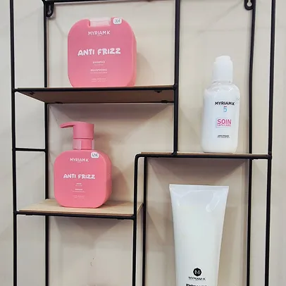 Produits capillaires Myriam K roses et blancs sur des étagères murales.